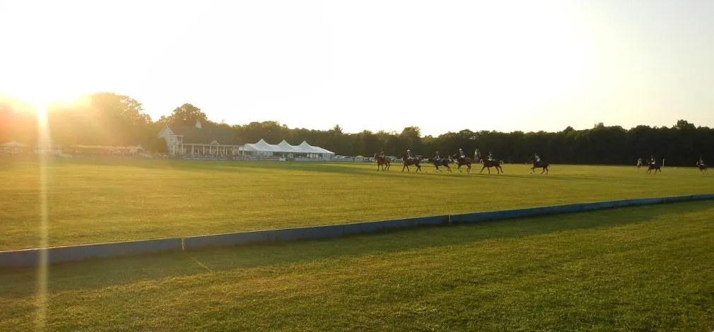 A polo match on Whitney Field at sunset, with the clubhouse and tents in the background